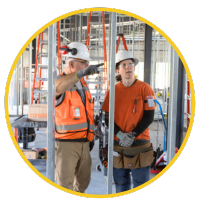 A male and female electrician stand next to each other examining the interior of a building under construction.