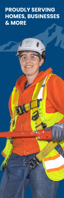 Female electrician smiling and wearing a hard hat while holding tools.