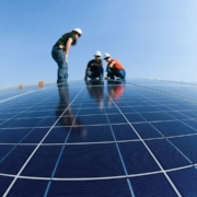 Three electricians work to install solar panels on the roof of a commercial property.
