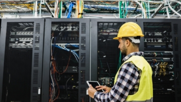 Commercial electrician in hard hat and safety vest checks the performance of a data center's servers.