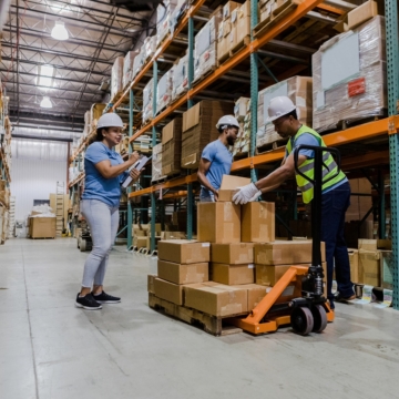 Three workers in a warehouse using a forklift to move boxes.