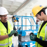 Two electricians in safety gear install wiring in a commercial building.