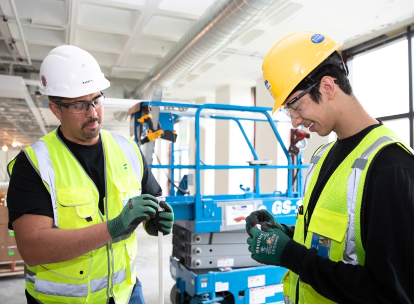 Two electricians in safety gear install wiring in a commercial building.