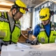 Two electrical contractors review blueprints of a commercial building.