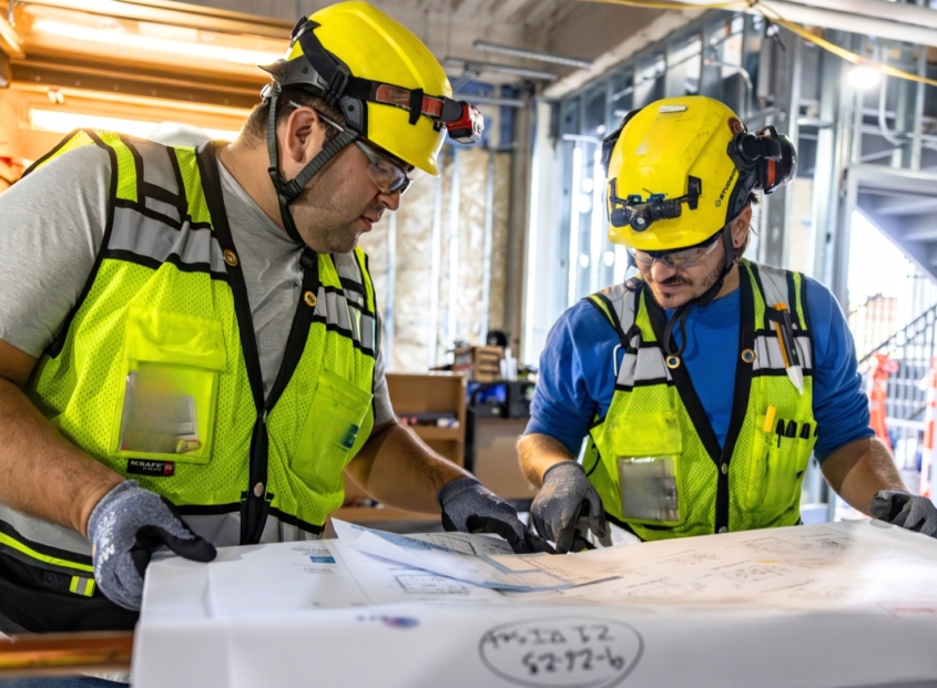 Two electrical contractors review blueprints of a commercial building.