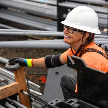 Smiling female electrician wearing a white helmet and orange shirt.