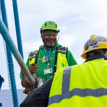 Two male electricians in yellow safety vests talking.