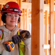 Woman construction worker wearing a red construction hat and using a drill on a house construction project.