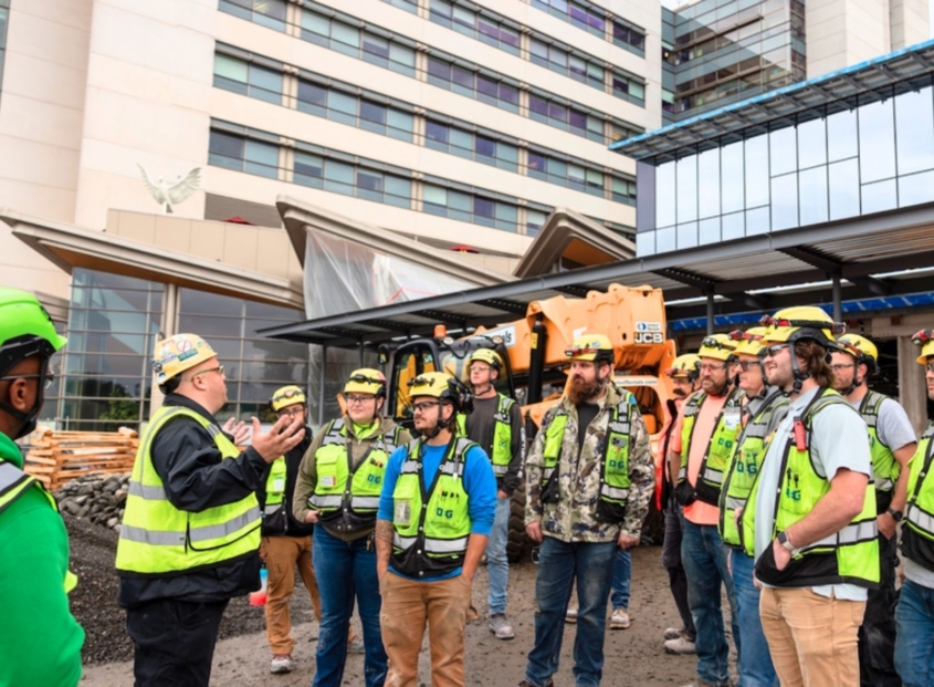 Group of construction workers and commercial electricians stand in front of a building under construction.