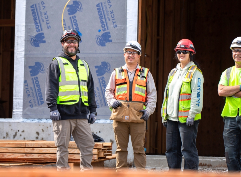 Four IBEW Local 48 union members wearing safety gear standing outside of a commercial building under construction.
