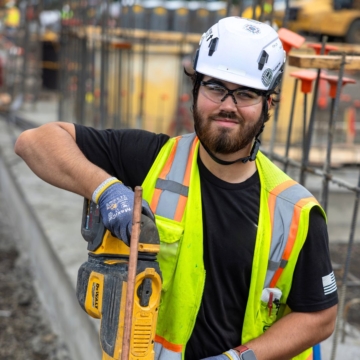 Electrical contractor in safety vest, goggles, and hard hat holding an electrical panel monitoring device.