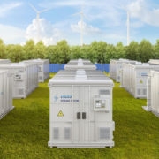 Multiple white energy storage systems (ESS) in a green field with trees in the background.