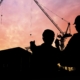 Orange and yellow sky with black shadows of construction machinery and electrical workers.