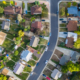 Aerial photo of suburban neighborhood with homes, trees, roads, and cars.