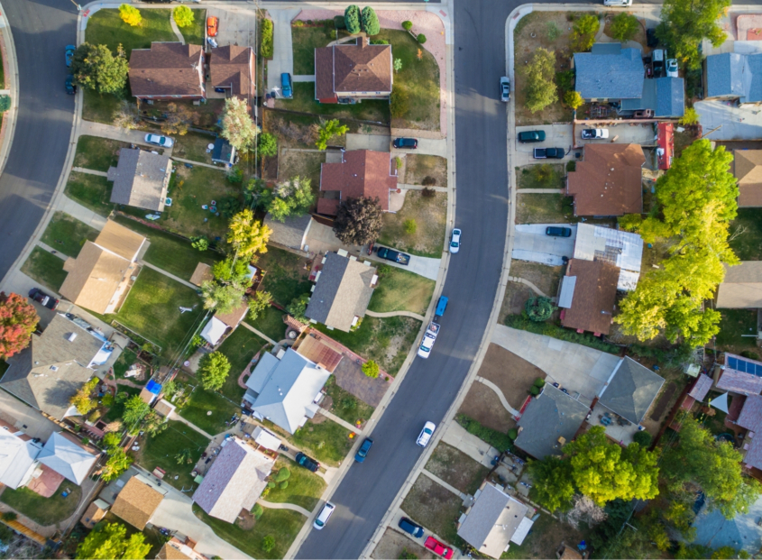 Aerial photo of suburban neighborhood with homes, trees, roads, and cars.