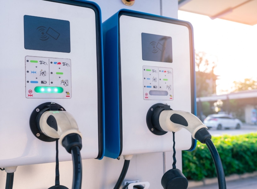 Electric vehicle charging stations with user panels and charging cables in a row.