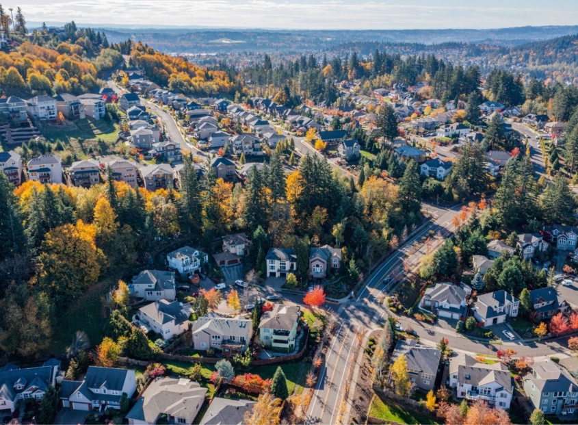 Aerial view of a suburban neighborhood with streets, houses, and autumn trees.