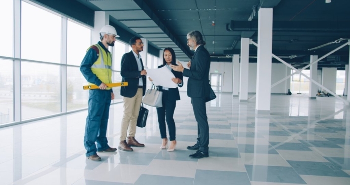 Group of four men and women reviewing architectural plans in a newly constructed office building.