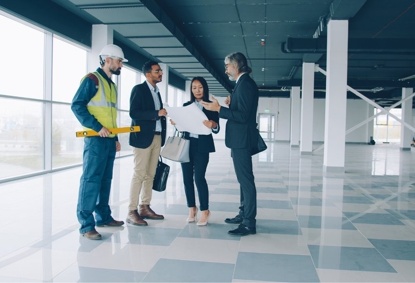 Group of four men and women reviewing architectural plans in a newly constructed office building.