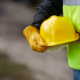 Close-up of a construction worker in a neon green safety vest and leather work gloves holding a yellow hard hat at a job site