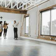 Realtor shows two people the inside of a commercial building with large windows and wood floor.