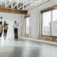 Realtor shows two people the inside of a commercial building with large windows and wood floor.