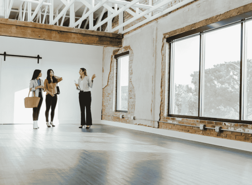 Realtor shows two people the inside of a commercial building with large windows and wood floor.