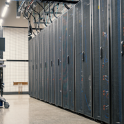 Interior of a data center with rows of server racks, cable management overhead, and a mobile workstation with a monitor in the aisle.
